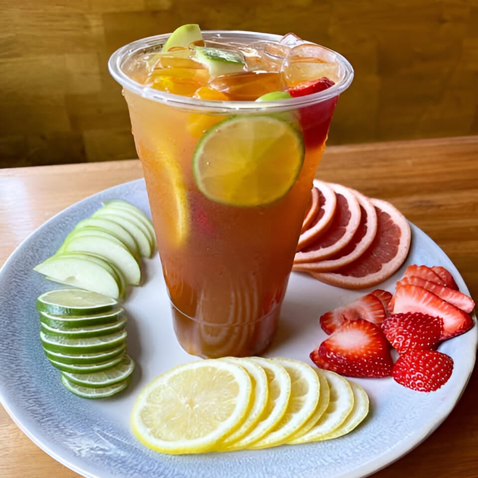 Fruity iced tea with sliced apples, limes, lemons, grapefruit, and strawberries on a plate.