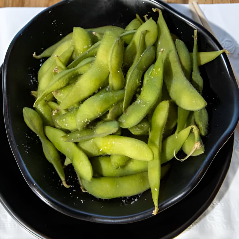 A black bowl filled with bright green, salted edamame pods, ready to be enjoyed.