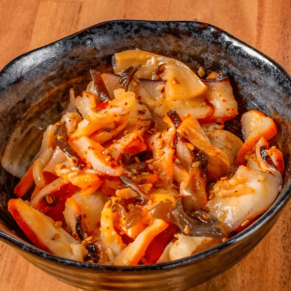 A black bowl filled with spicy seasoned squid salad, garnished with sesame seeds.