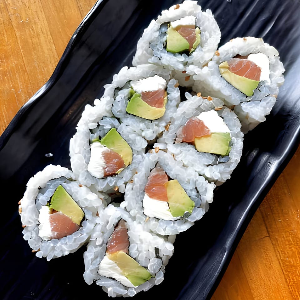 Eight sushi rolls with salmon, avocado, and cream cheese on a black rectangular plate.