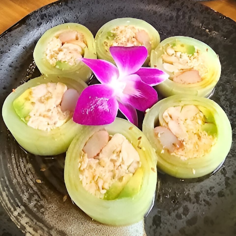 Six Little Ginger cucumber rolls with avocado, crab, and a purple orchid on a dark plate.