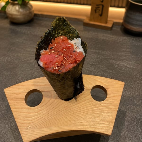 A hand roll temaki sushi with tuna, rice, and sesame seeds on a wooden stand.