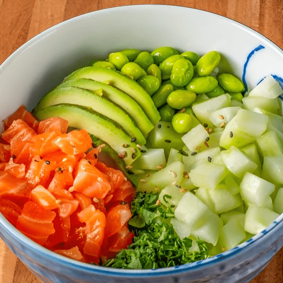 A colorful poke bowl with diced salmon, sliced avocado, edamame, and cucumber in a white bowl.